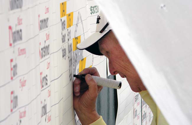 Dave Chapple posts scores on the big board under a sheet of plastic to keep the rain at bay on Saturday at Good Park.